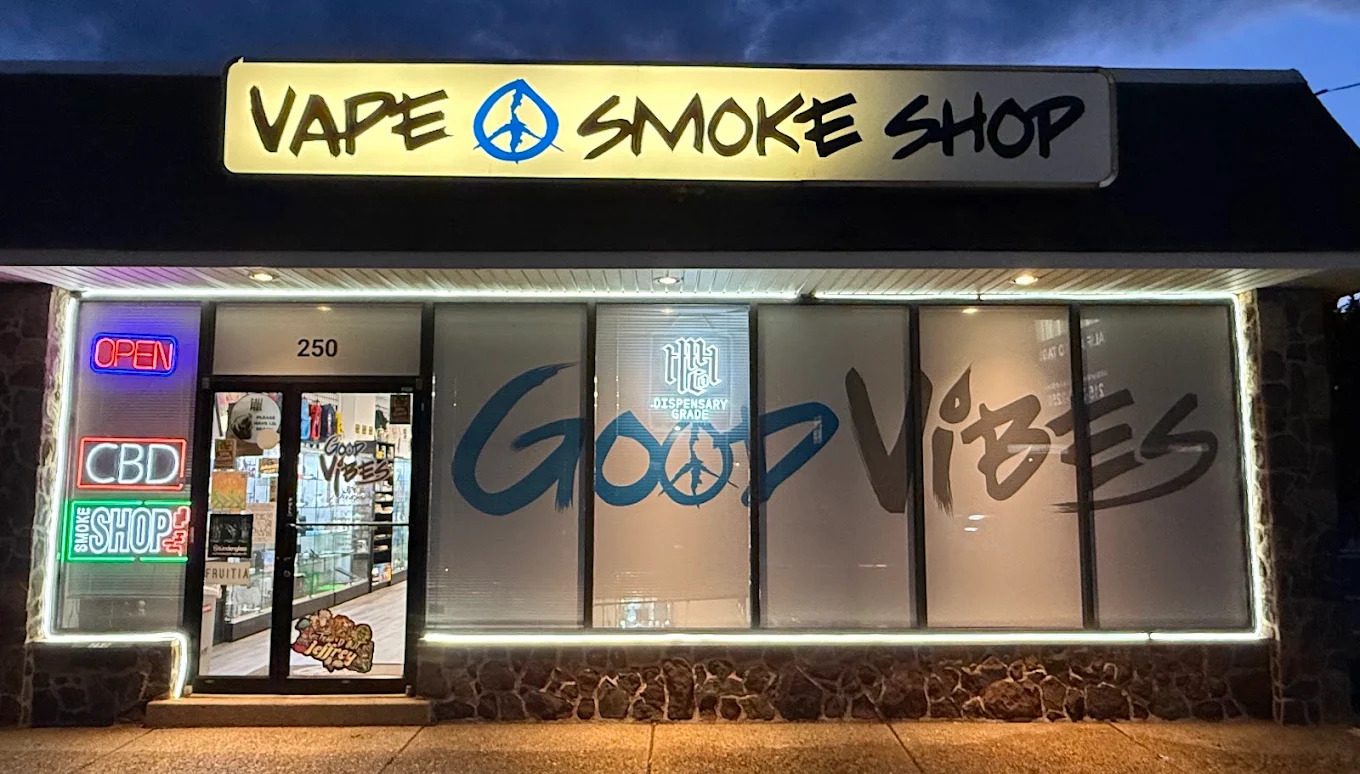 A Good Vibes shop at night, with its lit Vape & Smoke Shop sign and Good Vibes lettering across the windows